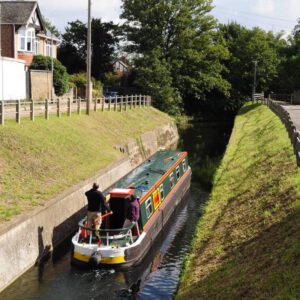 Bright coloured narrowboat navigating a lock on a calm canal.