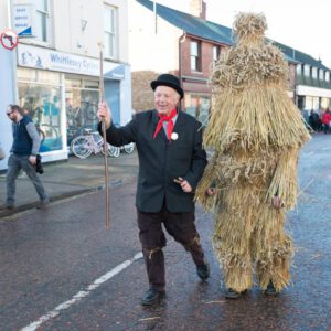 A man in traditional costume and a straw figure parade in Whittlesey for charity event.