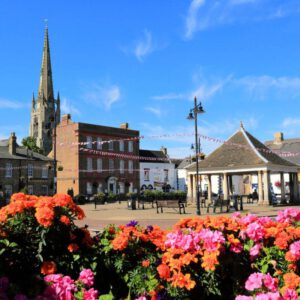 Vibrant town square with flower beds, historic buildings, and a church spire in Whittlesey, fostering community and charity events.